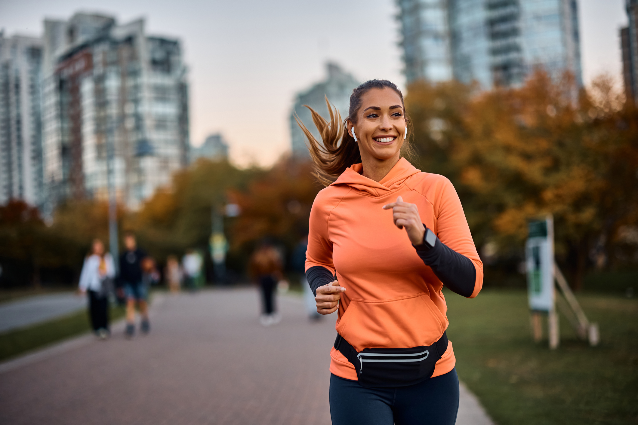 Young happy athletic woman listening music on earphones while jogging in the park.